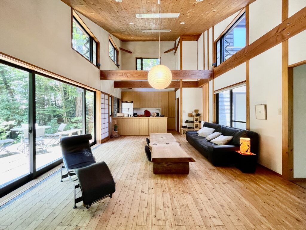 自然素材の家 別荘 注文住宅専門の一級建築士事務所探彩工房建築設計事務所のモデルハウス 静岡県裾野市十里木高原別荘地に建築 中庭、土間、ウッドデッキなど東西南北と高窓からの最高で明るく風通しのいい設計プラン。 全室壁天井は消臭調湿効果が高い珪藻土、床は無垢の桧のフローリングなど天然素材仕上げ。 夏や梅雨時は湿気や熱を外に排気、冬は太陽熱で温めた外気を床下に送り換気をしながら床暖房するソーラーシステムそよ風で家中足元から暖かくします。 自然素材とソーラーシステムそよ風の相乗効果で湿気が少なく夏涼しく冬暖かい明るく風通しのいいパッシブデザインの別荘・注文住宅です。 画像はウッドデッキと中庭が隣接した土間に薪ストーブかある吹抜けのリビング。 杉の一枚もののテーブルやアルフレックスのベンゴディのソファーなど好きなものに囲まれた暮らしを楽しんでいます。 木の香りやぬくもりなど自然素材の家専門の設計事務所ならではの心地よい空間デザインです。