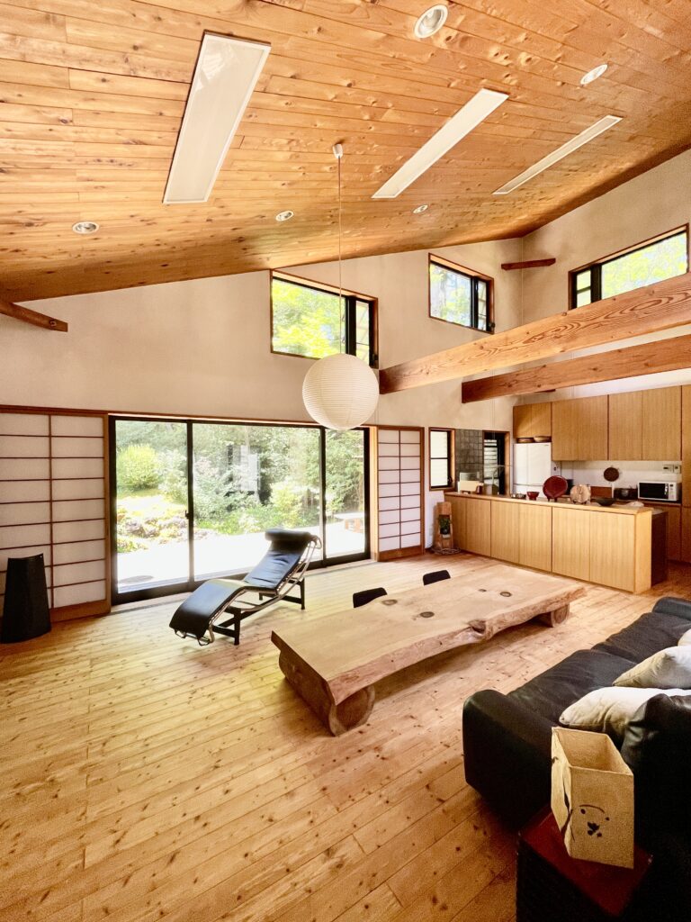 自然素材の家 別荘 注文住宅専門の一級建築士事務所探彩工房建築設計事務所のモデルハウス 静岡県裾野市十里木高原別荘地に建築 中庭、土間、ウッドデッキなど東西南北と高窓からの最高で明るく風通しのいい設計プラン。 全室壁天井は消臭調湿効果が高い珪藻土、床は無垢の桧のフローリングなど天然素材仕上げ。 夏や梅雨時は湿気や熱を外に排気、冬は太陽熱で温めた外気を床下に送り換気をしながら床暖房するソーラーシステムそよ風で家中足元から暖かくします。 自然素材とソーラーシステムそよ風の相乗効果で湿気が少なく夏涼しく冬暖かい明るく風通しのいいパッシブデザインの別荘・注文住宅です。 画像はウッドデッキと中庭が隣接した土間に薪ストーブかある吹抜けのリビング。 杉の一枚もののテーブルやアルフレックスのベンゴディのソファーなど好きなものに囲まれた暮らしを楽しんでいます。 木の香りやぬくもりなど自然素材の家専門の設計事務所ならではの心地よい空間デザインです。
