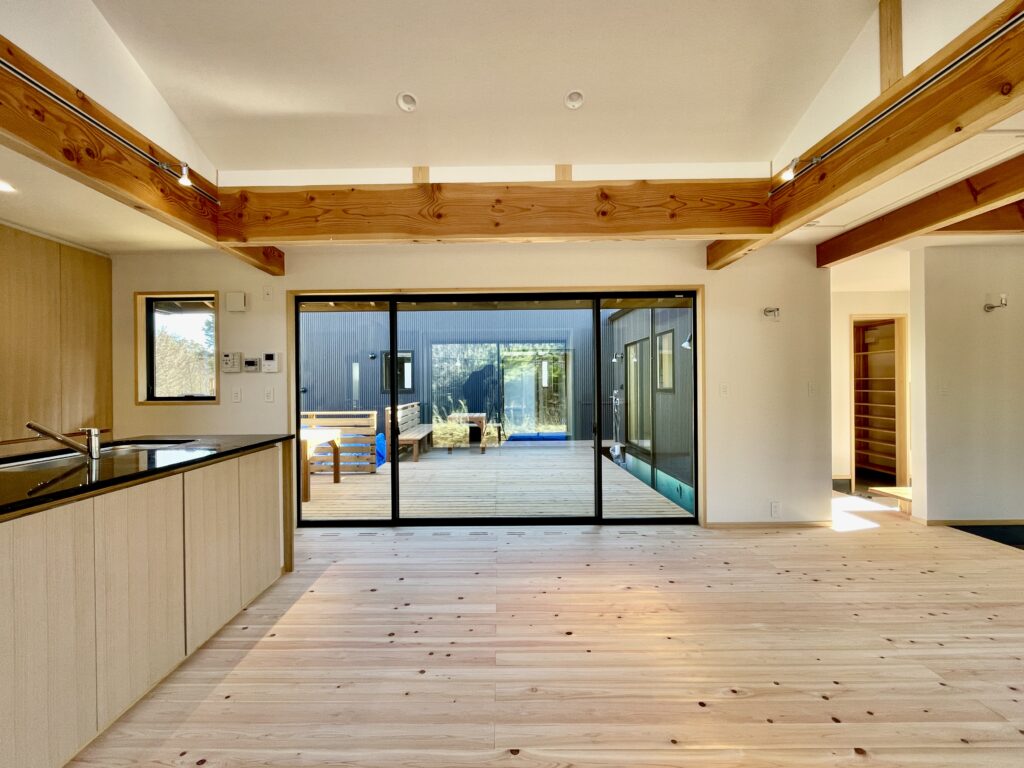 [山梨県八ヶ岳南麓北杜市長坂に建築したパッシブデザインの自然素材の家　建築設計施工事例]自然素材の家　別荘　注文住宅専門の建築設計事務所と建てるソーラーシステムそよ風で床暖房するサステナブルな環境共生住宅 コの字型間取りプラン 画像はこの塀で目隠ししたウッドデッキの中庭が隣接する吹抜けのLDK 明るく風通しのいい夏涼しく冬暖かいリビングです