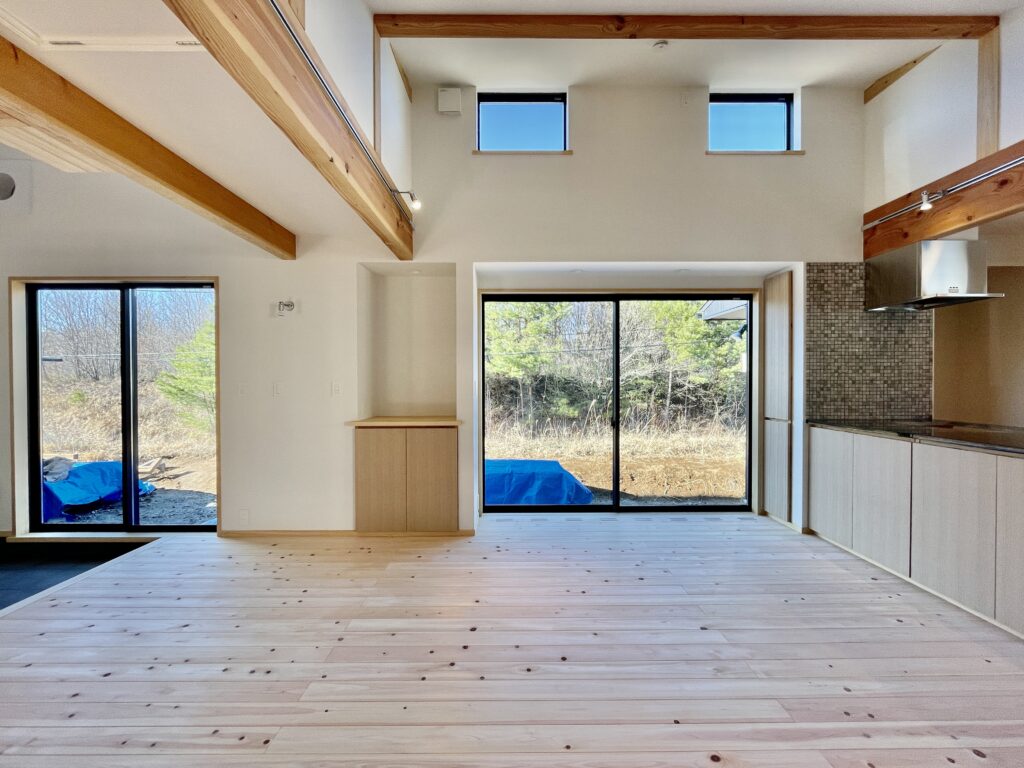 [山梨県八ヶ岳南麓北杜市長坂に建築したパッシブデザインの自然素材の家　建築設計施工事例]自然素材の家　別荘　注文住宅専門の建築設計事務所と建てるソーラーシステムそよ風で床暖房するサステナブルな環境共生住宅 コの字型間取りプラン 画像はウッドデッキの北側のバックヤードが隣接する吹抜けのLDK 玄関続きの土間には薪ストーブを設置 高窓からの通風と彩光で明るく風通しのいい夏涼しく冬暖かいリビングです