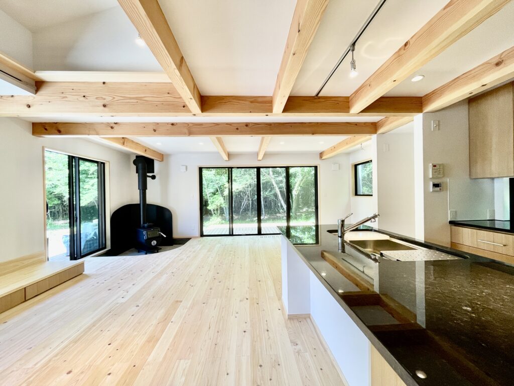 静岡県東部裾野市十里木高原に建築したソーラーシステムそよ風で床暖房するパッシブデザインのサステナブルな自然素材の家 ビルとインナーガレージ　広いウッドデッキ　富士山一望のロフト　リビング土間に薪ストーブなど家の中もアウトドアも楽しめる環共生住宅 画像はウッドデッキから出入りできる土間に薪ストーブを設置した吹抜けのリビング
