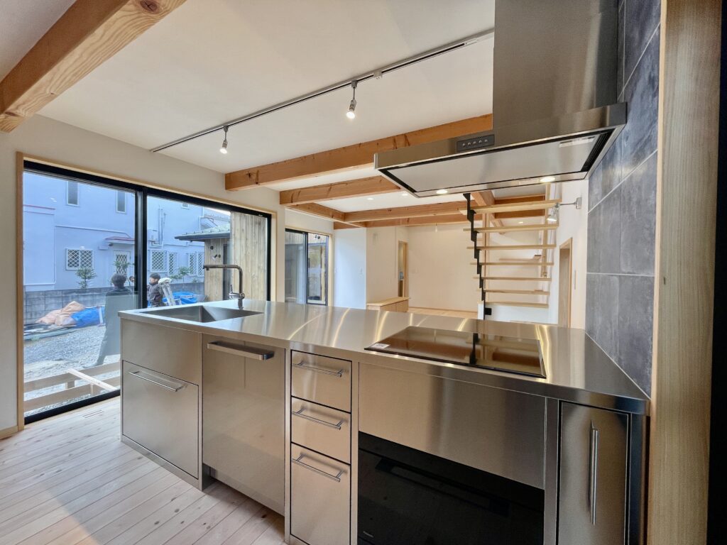 神奈川県鎌倉市西鎌倉に建築したL字型間取り設計の自然素材の家。夏や梅雨時は湿気や熱を排気し、冬は太陽熱で温めた外気を床下に送り換気をしながら床暖房するソーラーシステムそよ風で家中足元から暖かくします。壁天井は消臭調湿効果が高い珪藻土、床は桧フローリングなど天然素材仕上げ。自然素材とソーラーシステムそよ風の相乗効果で湿気が少なく夏涼しく冬暖かいパッシブデザインの環境共生住宅です。 全室収納は造り付けで作成したのでスッキリものが片付き使い勝手と住み心地がいいサステナブルハウス。 画像はオーダーで作成したステンレスキッチン。ユーロスタイルのIHクッキングヒーター、ボッシュの食洗機、グローエの引き出しシャワー水栓、ステンレスの換気扇など好きなパーツを組み合わせ。