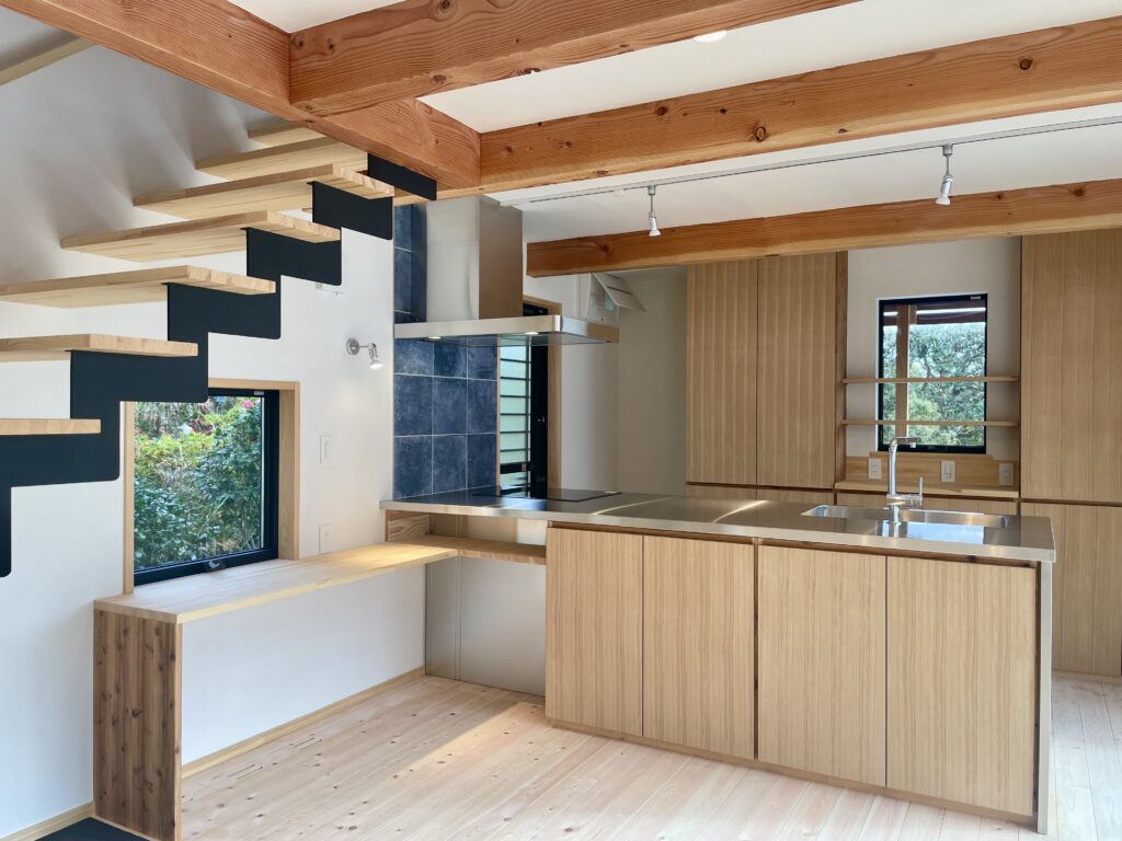 神奈川県鎌倉市西鎌倉に建築したL字型間取り設計の自然素材の家。夏や梅雨時は湿気や熱を排気し、冬は太陽熱で温めた外気を床下に送り換気をしながら床暖房するソーラーシステムそよ風で家中足元から暖かくします。壁天井は消臭調湿効果が高い珪藻土、床は桧フローリングなど天然素材仕上げ。自然素材とソーラーシステムそよ風の相乗効果で湿気が少なく夏涼しく冬暖かいパッシブデザインの環境共生住宅です。 全室収納は造り付けで作成したのでスッキリものが片付き使い勝手と住み心地がいいサステナブルハウス。 画像は書斎コーナーと一体型で作成したステンレスキッチン。ユーロスタイルのIHクッキングヒーター、ボッシュの食洗機、グローエの引き出しシャワー水栓、ステンレスの換気扇など好きなパーツをで作成。