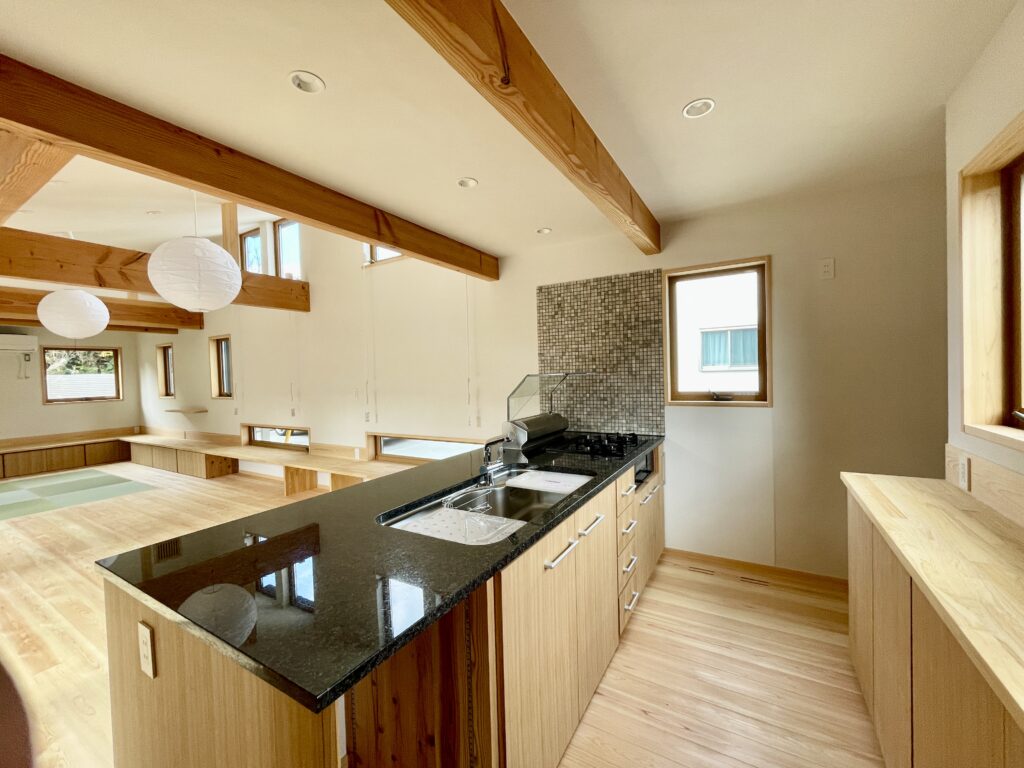 静岡県東部沼津市に建築したコの字型間取り設計の平家の自然素材の家。夏や梅雨時は湿気や熱を排気し、冬は太陽熱で温めた外気を床下に送り換気をしながら床暖房するソーラーシステムそよ風で家中足元から暖かくします。壁天井は消臭調湿効果が高い珪藻土、床は桧フローリングなど天然素材仕上げ。自然素材とソーラーシステムそよ風の相乗効果で湿気が少なく夏涼しく冬暖かいパッシブデザインの環境共生住宅です。 全室収納は造り付けで作成したのでスッキリものが片付き使い勝手と住み心地がいいサステナブルハウス。 画像は造り付けで作成した御影石の天板の造作キッチンと造作食器棚。東西南北と高窓からの通風と採光で明るく風通しのいいリビングです。