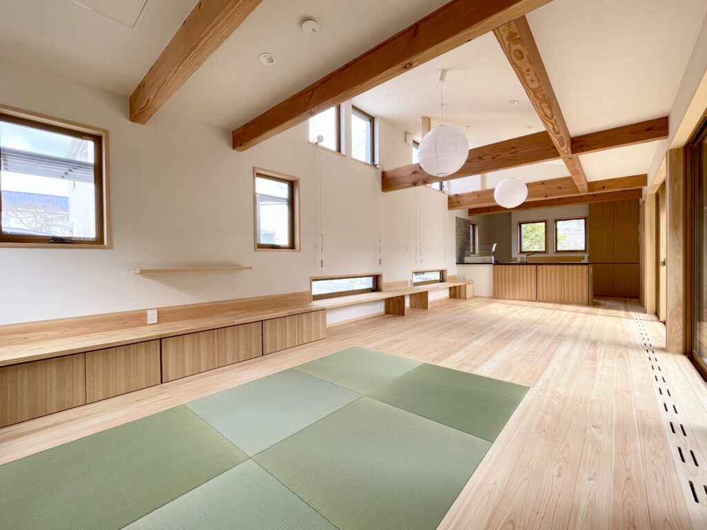 静岡県東部沼津市に建築したコの字型間取り設計の平家の自然素材の家。夏や梅雨時は湿気や熱を排気し、冬は太陽熱で温めた外気を床下に送り換気をしながら床暖房するソーラーシステムそよ風で家中足元から暖かくします。壁天井は消臭調湿効果が高い珪藻土、床は桧フローリングなど天然素材仕上げ。自然素材とソーラーシステムそよ風の相乗効果で湿気が少なく夏涼しく冬暖かいパッシブデザインの環境共生住宅です。 全室収納は造り付けで作成したのでスッキリものが片付き使い勝手と住み心地がいいサステナブルハウス。 画像は東西南北と高窓からの通風と採光で明るく風通しのいい中庭が隣接した吹抜けリビング。