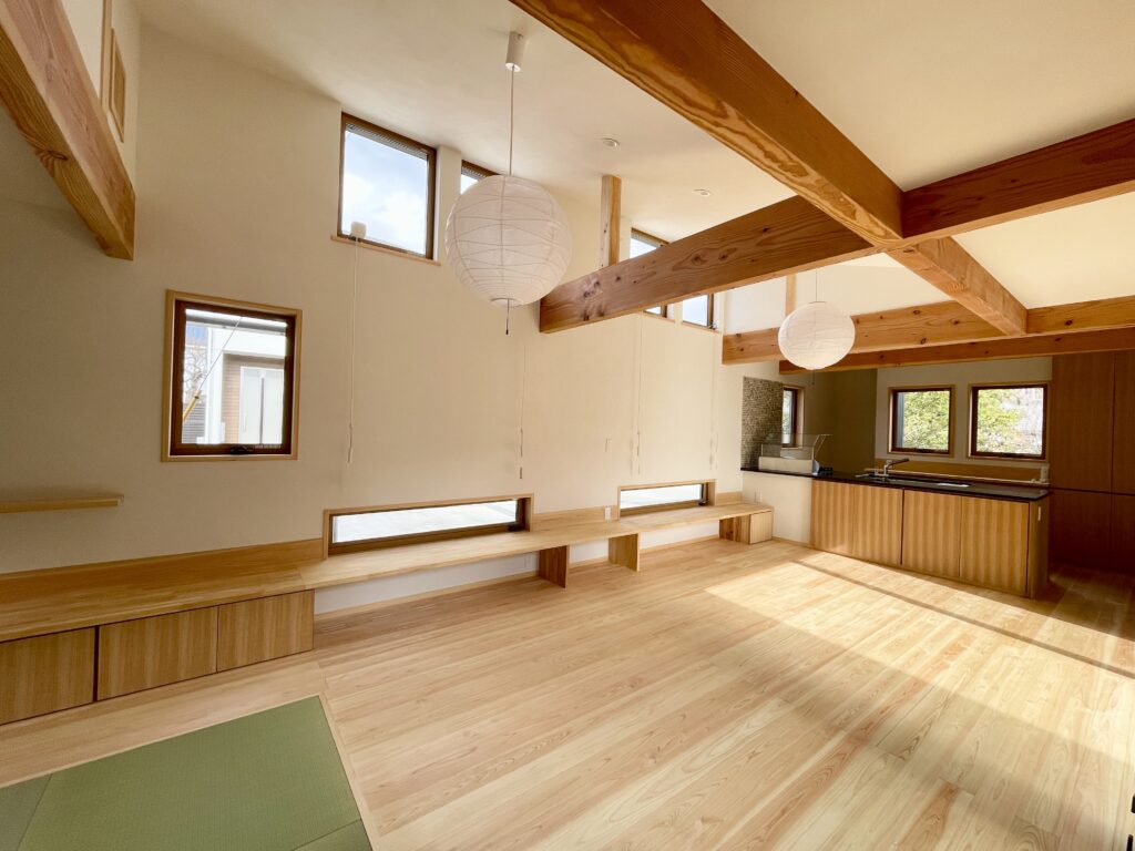 静岡県東部沼津市に建築したコの字型間取り設計の平家の自然素材の家。夏や梅雨時は湿気や熱を排気し、冬は太陽熱で温めた外気を床下に送り換気をしながら床暖房するソーラーシステムそよ風で家中足元から暖かくします。壁天井は消臭調湿効果が高い珪藻土、床は桧フローリングなど天然素材仕上げ。自然素材とソーラーシステムそよ風の相乗効果で湿気が少なく夏涼しく冬暖かいパッシブデザインの環境共生住宅です。 全室収納は造り付けで作成したのでスッキリものが片付き使い勝手と住み心地がいいサステナブルハウス。 画像は東西南北と高窓からの通風と採光で明るく風通しのいい中庭が隣接した吹抜けリビング。
