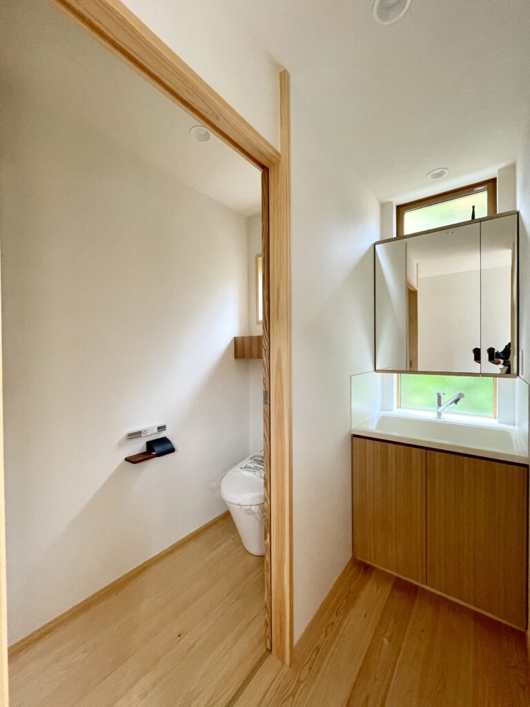 静岡県東部沼津市に建築したコの字型間取り設計の平家の自然素材の家。夏や梅雨時は湿気や熱を排気し、冬は太陽熱で温めた外気を床下に送り換気をしながら床暖房するソーラーシステムそよ風で家中足元から暖かくします。壁天井は消臭調湿効果が高い珪藻土、床は桧フローリングなど天然素材仕上げ。自然素材とソーラーシステムそよ風の相乗効果で湿気が少なく夏涼しく冬暖かいパッシブデザインの環境共生住宅です。 全室収納は造り付けで作成したのでスッキリものが片付き使い勝手と住み心地がいいサステナブルハウス。 画像は人工大理石のキッチンシンクを利用した手元が明るい造作洗面化粧台。鏡収納扉の中にコンセント設置。