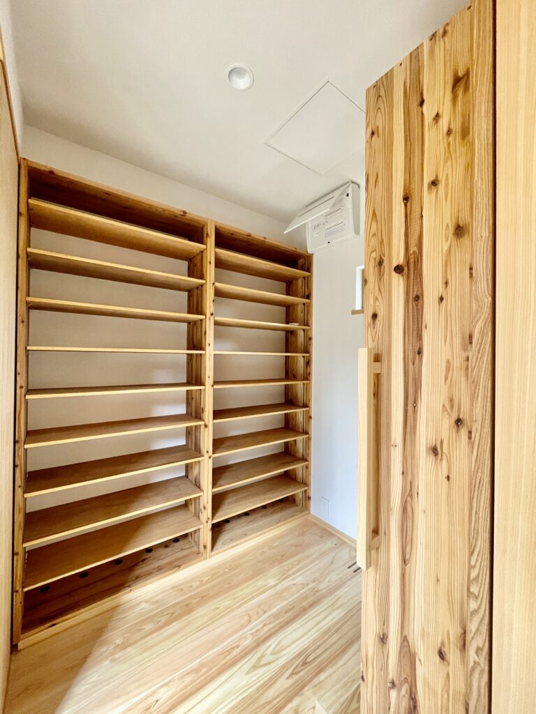 静岡県東部沼津市に建築したコの字型間取り設計の平家の自然素材の家。夏や梅雨時は湿気や熱を排気し、冬は太陽熱で温めた外気を床下に送り換気をしながら床暖房するソーラーシステムそよ風で家中足元から暖かくします。壁天井は消臭調湿効果が高い珪藻土、床は桧フローリングなど天然素材仕上げ。自然素材とソーラーシステムそよ風の相乗効果で湿気が少なく夏涼しく冬暖かいパッシブデザインの環境共生住宅です。 全室収納は造り付けで作成したのでスッキリものが片付き使い勝手と住み心地がいいサステナブルハウス。 画像は玄関土間続きのウォークスルーシューズクローゼット。