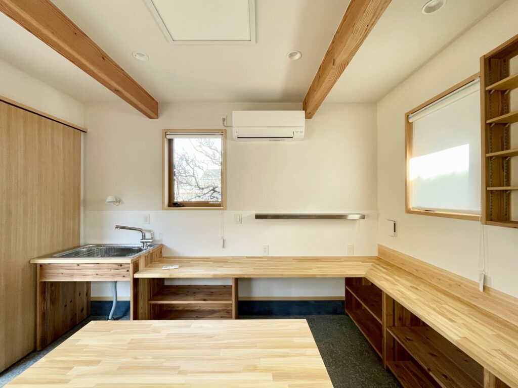 静岡県東部沼津市に建築したコの字型間取り設計の平家の自然素材の家。夏や梅雨時は湿気や熱を排気し、冬は太陽熱で温めた外気を床下に送り換気をしながら床暖房するソーラーシステムそよ風で家中足元から暖かくします。壁天井は消臭調湿効果が高い珪藻土、床は桧フローリングなど天然素材仕上げ。自然素材とソーラーシステムそよ風の相乗効果で湿気が少なく夏涼しく冬暖かいパッシブデザインの環境共生住宅です。 全室収納は造り付けで作成したのでスッキリものが片付き使い勝手と住み心地がいいサステナブルハウス。 画像は玄関土間続きの陶芸アトリエ。ろくろが２台置けるスペースがあり収納棚や展示だなは造り付けで作成。