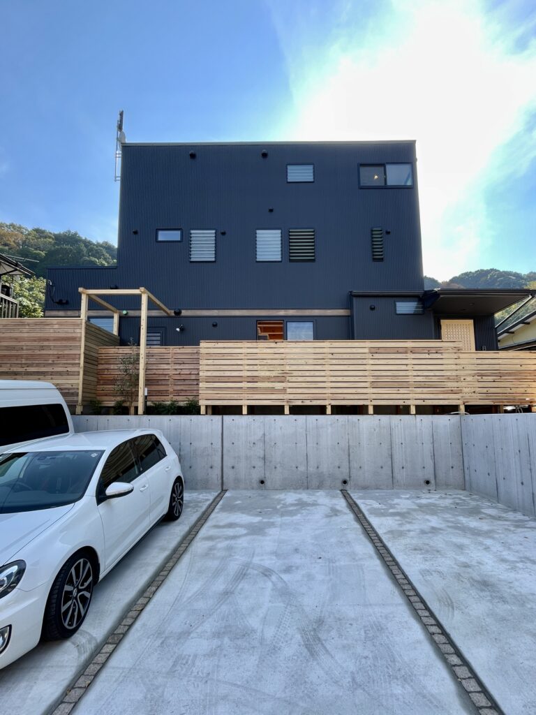 外観は縦ストライプのガルバリウムでシンプルモダンデザイン。玄関続きのバックヤードはウッドデッキで木製の目隠し塀でプライバシー確保。