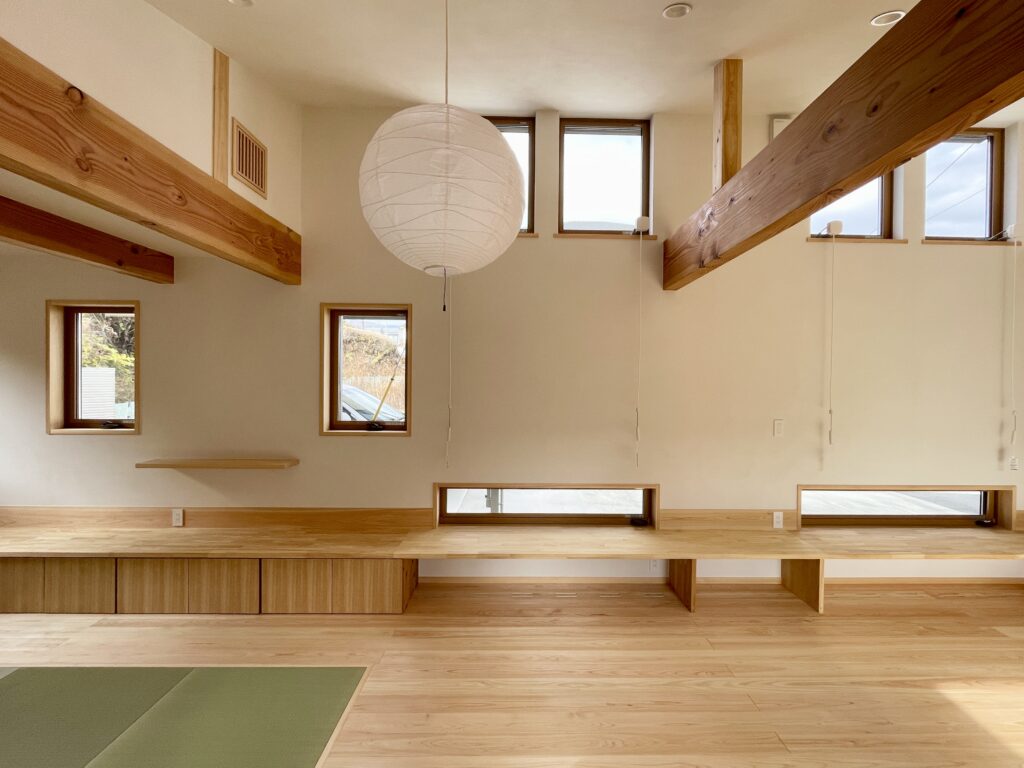 静岡県東部沼津市に建築したコの字型間取りの自然素材の家 。梅雨時や夏は熱気や湿気を排気し冬は太陽熱で温めた外気を床下に送り換気をしながら床暖房するソーラーシステムそよ風で家中足元から暖かい環境共生住宅です。 全室壁天井は消臭調湿効果が高い珪藻土床は桧のフローリングなど天然素材仕上げ 。自然素材とソーラーシステムそよ風の相乗効果で湿気が少なく夏涼しく冬暖かい明るく風通しのいいパッシブデザインの注文住宅 。全室収納を造り付けで作成しスッキリものが片付き使い勝手と居心地がいいサステナブルハウス 。画像は冬は太陽熱で床暖房するソーラーシステムで足元から暖かく、夏は東西南北と高窓からの通風と採光で明るく風通しのいい吹抜けのリビング　沼津市の自然素材の家