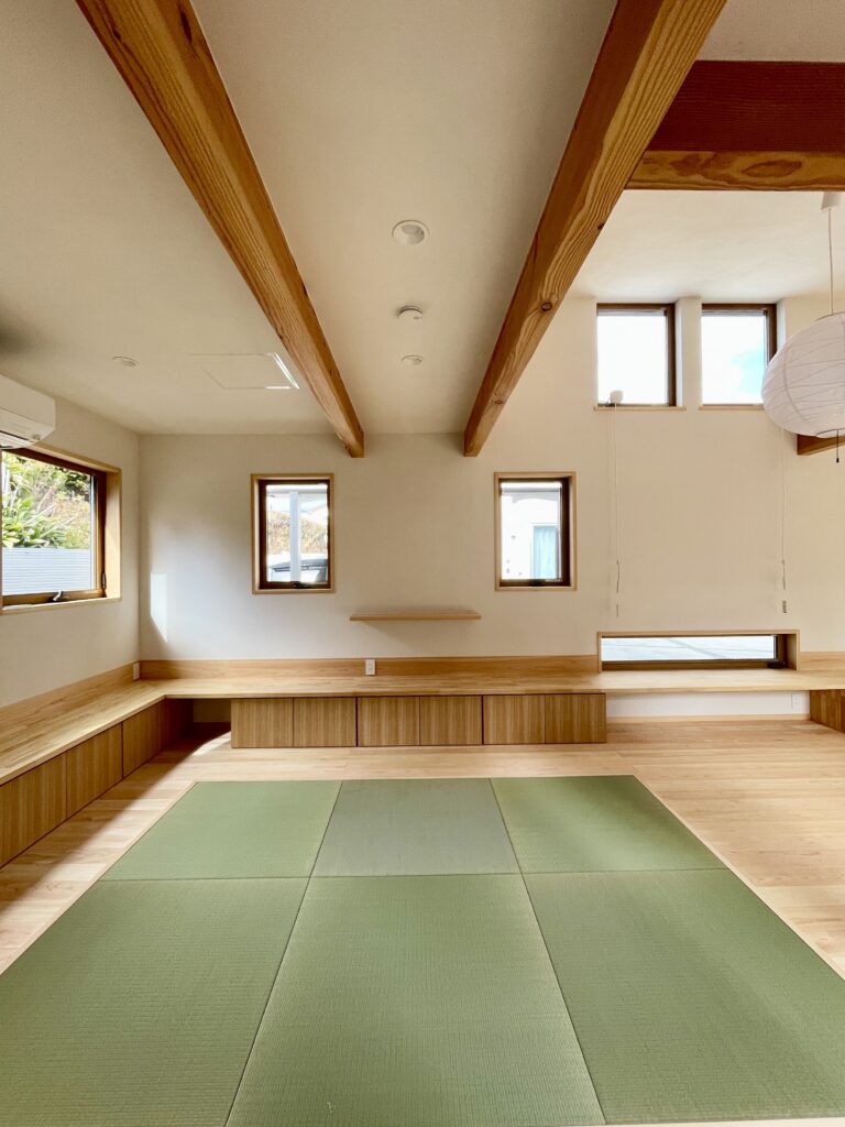 静岡県東部沼津市に建築したコの字型間取りの自然素材の家 。梅雨時や夏は熱気や湿気を排気し冬は太陽熱で温めた外気を床下に送り換気をしながら床暖房するソーラーシステムそよ風で家中足元から暖かい環境共生住宅です。 全室壁天井は消臭調湿効果が高い珪藻土床は桧のフローリングなど天然素材仕上げ 。自然素材とソーラーシステムそよ風の相乗効果で湿気が少なく夏涼しく冬暖かい明るく風通しのいいパッシブデザインの注文住宅 。全室収納を造り付けで作成しスッキリものが片付き使い勝手と居心地がいいサステナブルハウス 。画像は冬は太陽熱で床暖房するソーラーシステムで足元から暖かく、夏は東西南北と高窓からの通風と採光で明るく風通しのいい吹抜けのリビング　沼津市の自然素材の家